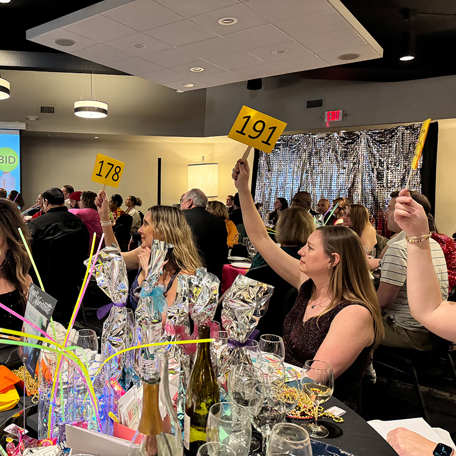 paddle raise gala 2025 women raising paddles at table during paddle raise at 90s prom gala 2025